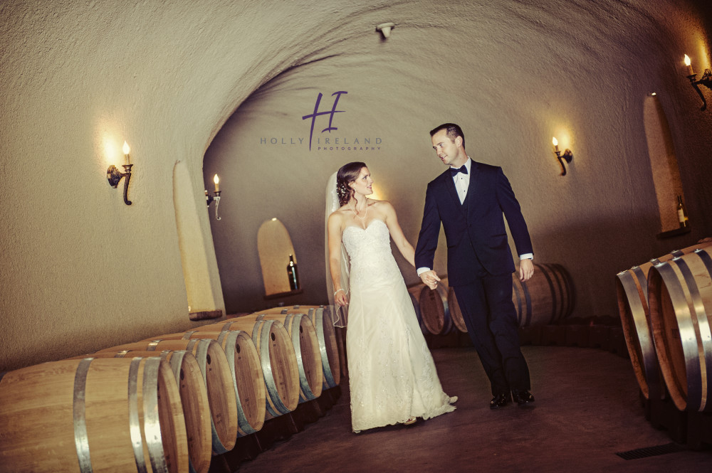 Bride and groom walking through the barrel room in a winery in Napa  www.hollyireland.com